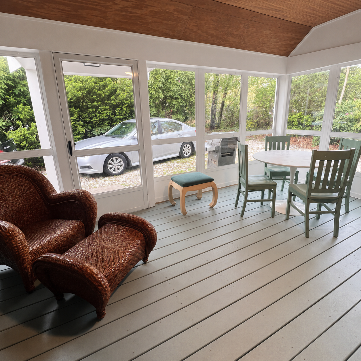 Screened sunroom with wicker seating, dining table, and garden views